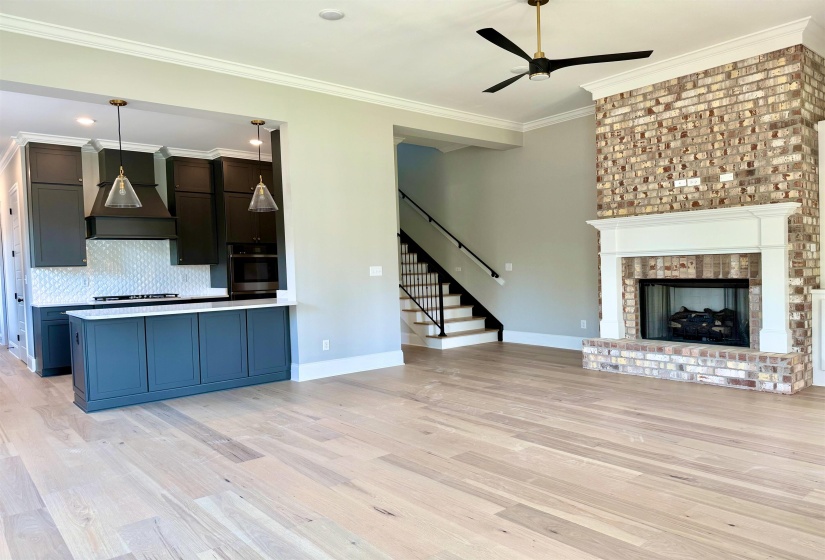 Unfurnished living room featuring ornamental molding, light wood-style flooring, ceiling fan, stairs, and a brick fireplace