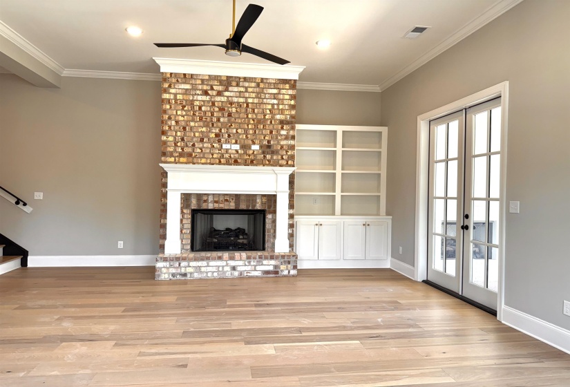 Unfurnished living room featuring french doors, crown molding, a brick fireplace, light wood-style floors, and ceiling fan
