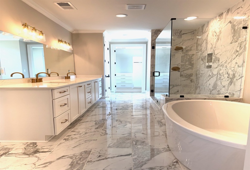 Full bathroom featuring light marble finish floors, a shower stall, a soaking tub, double vanity, and ornamental molding