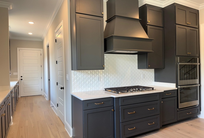 Kitchen with crown molding, light wood-style floors, custom range hood, light stone countertops, and recessed lighting