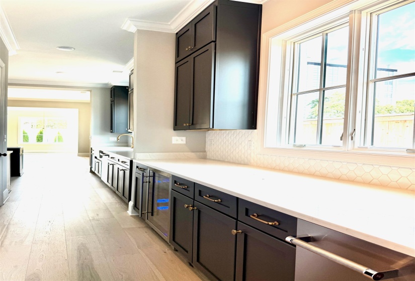 Kitchen with ornamental molding, light wood finished floors, dark cabinets, wine cooler, and light stone counters