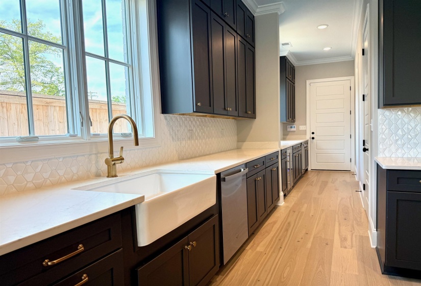 Kitchen with backsplash, light stone counters, ornamental molding, light wood-style floors, and dishwasher