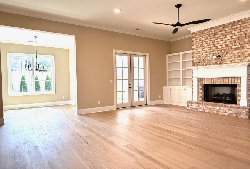 Unfurnished living room with plenty of natural light, ornamental molding, french doors, light wood-style flooring, and a brick fireplace
