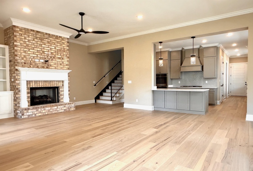 Unfurnished living room featuring ornamental molding, light wood-style flooring, ceiling fan, a fireplace, and stairs