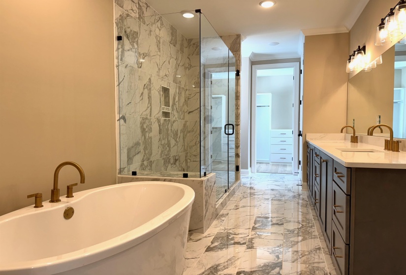 Bathroom featuring double vanity, a freestanding tub, a shower stall, light marble finish flooring, and recessed lighting
