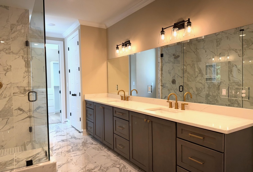 Full bathroom with light marble finish flooring, a marble finish shower, double vanity, and ornamental molding