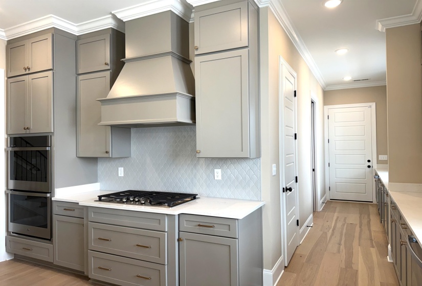 Kitchen with gray cabinetry, light wood finished floors, crown molding, stainless steel appliances, and light stone counters
