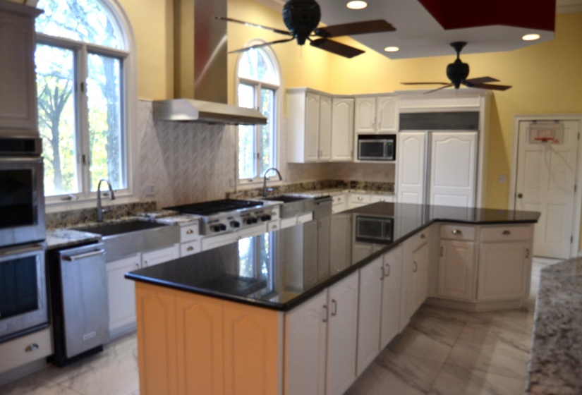 Kitchen featuring wall chimney range hood, ceiling fan, stainless steel appliances, a center island, and white cabinets