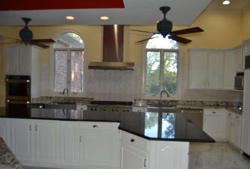 Kitchen with ceiling fan, white cabinets, wall chimney range hood, and recessed lighting