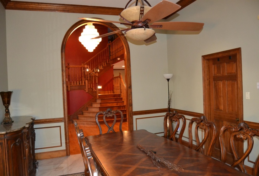 Dining area with a wainscoted wall, stairs, arched walkways, ceiling fan, and a decorative wall