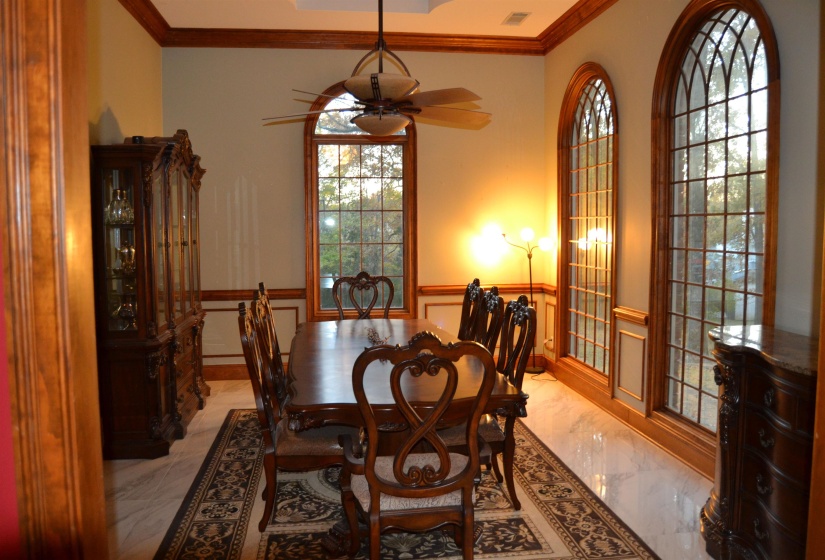 Dining room with ornamental molding, light marble finish flooring, a wainscoted wall, ceiling fan, and a decorative wall
