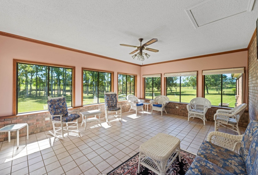 This inviting sunroom combines elegance and practicality with its tile floor, ceiling fan, and timeless brick wall. Windows on every side provide panoramic views and fill the room with natural light, creating a bright, airy space for relaxing.