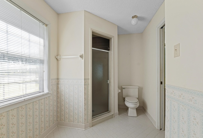 This light-filled primary bath features an enclosed shower, neutral tile floors, and a large window that enhances the sense of space.