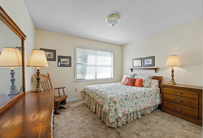 This cozy bedroom features a large window overlooking the yard, filling the space with natural light. The plush carpet adds warmth and coziness, creating a relaxing and welcoming environment.