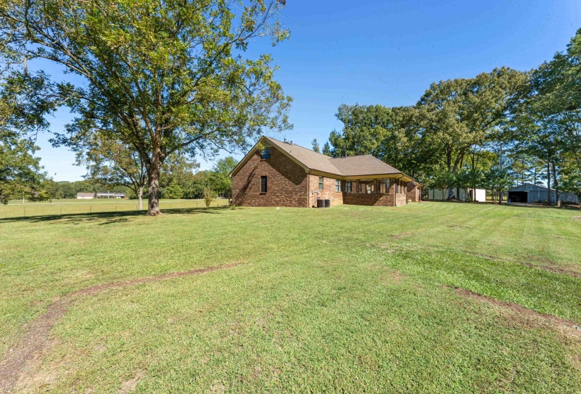 This rear view of the home showcases a small portion of the expansive property, with the show and barn visible in the distance. The setting highlights both functionality and serenity, offering endless possibilities for work, hobbies, or storage.