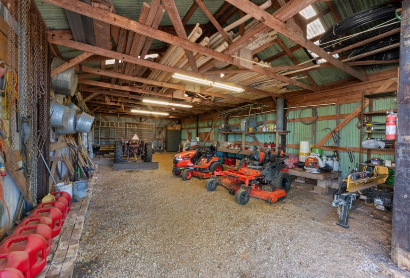 This barn/shop includes a gravel floor and a semi-enclosed covered lean-to, providing extra space for storage or work. The flexible layout accommodates a variety of practical uses on this large property.