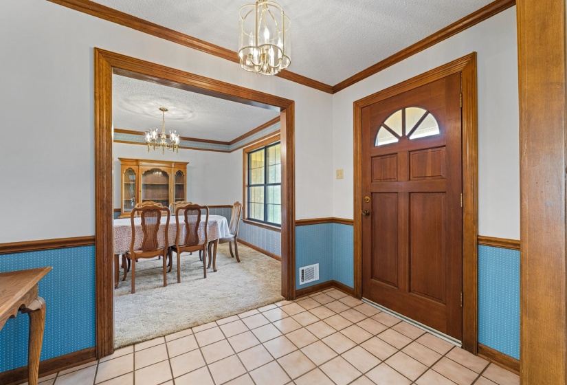 The entryway greets guests with a soft glow from a delicate chandelier, tile flooring underfoot, and sightlines that open to both the formal dining room and the main living area. It’s a welcoming introduction to a home designed for gathering.