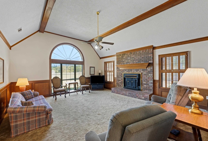 This spacious living room features soaring vaulted ceilings and a large window that bathes the space in natural light while overlooking the serene yard. The brick fireplace adds character and a cozy focal point, making this a comfortable gathering space.