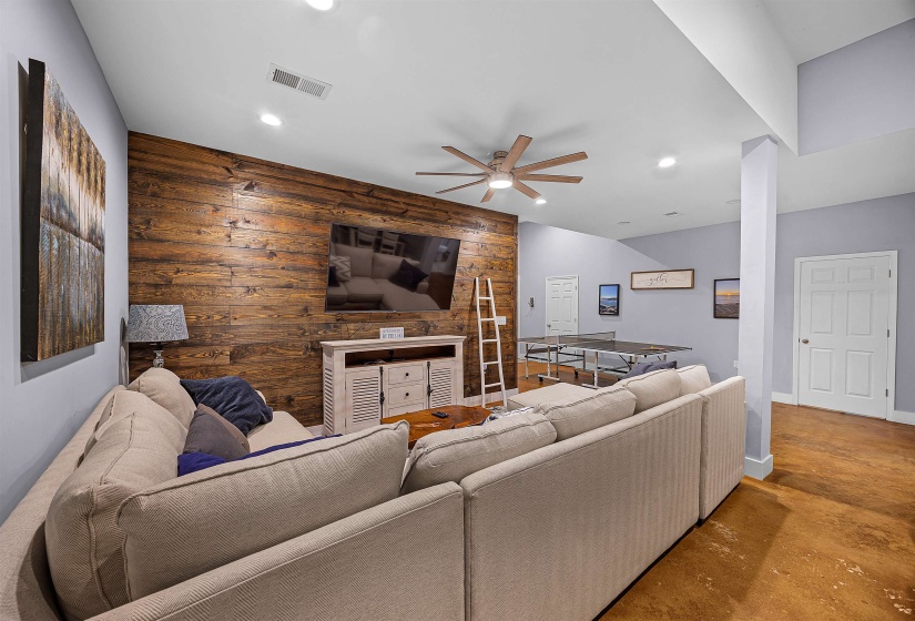 Living area with wood walls, concrete floors, an accent wall, a ceiling fan, and recessed lighting