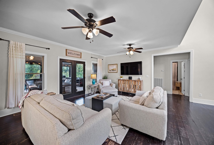 Living room featuring dark wood-style floors, crown molding, french doors, and ceiling fan