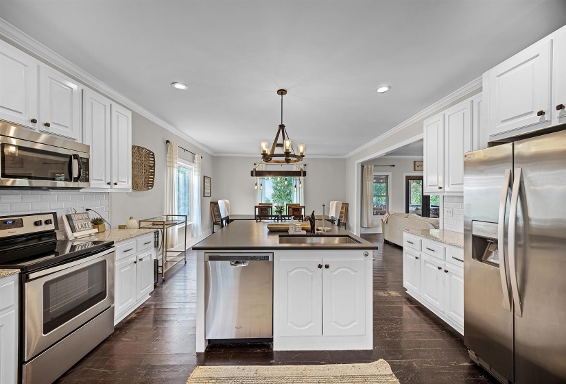 Kitchen with decorative backsplash, stainless steel appliances, white cabinets, a kitchen island with sink, and crown molding
