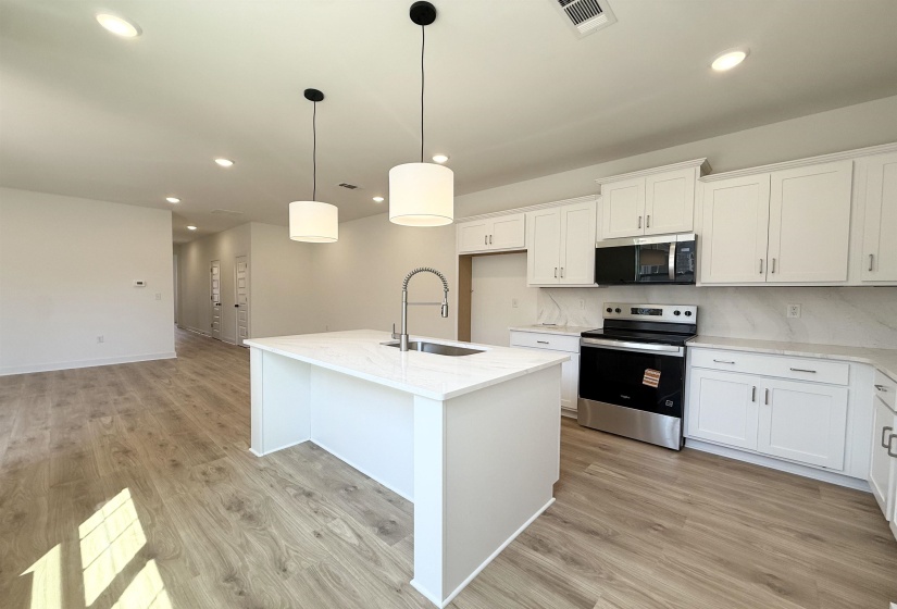 Kitchen featuring stainless steel appliances, an island with sink, light stone countertops, and white cabinetry