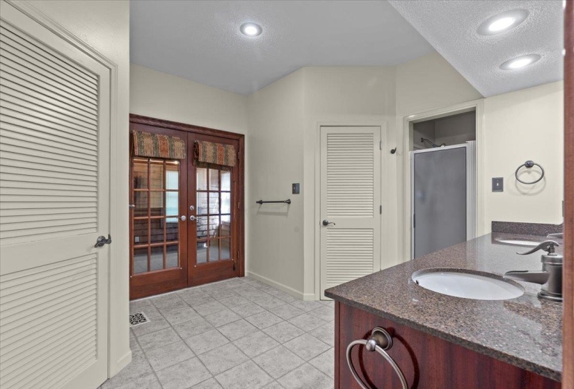 Bathroom featuring french doors, a closet, a textured ceiling, a stall shower, and double vanity