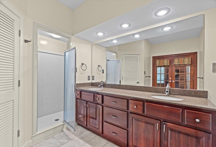 Bathroom featuring a closet, double vanity, a textured ceiling, recessed lighting, and a shower stall
