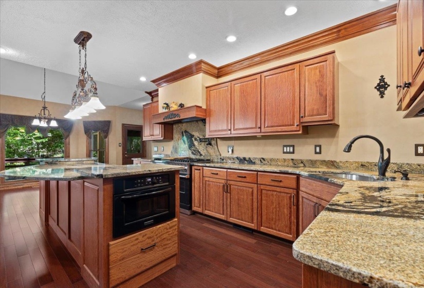 Kitchen with brown cabinetry, light stone counters, decorative light fixtures, oven, and high end stove
