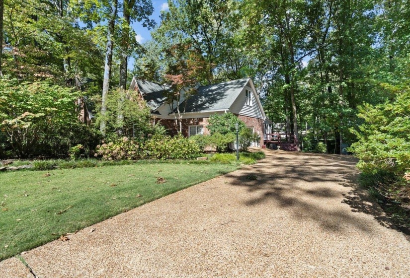 View of property exterior featuring brick siding, a yard, view of scattered trees, and driveway