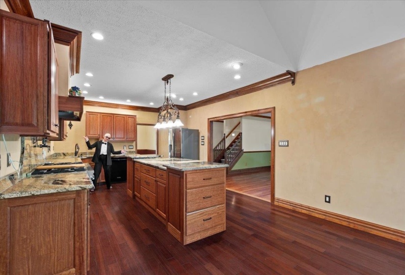 Kitchen with light stone countertops, dark wood-style floors, crown molding, brown cabinets, and decorative light fixtures
