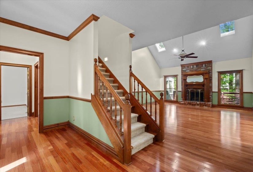 Staircase featuring a brick fireplace, wood finished floors, a skylight, high vaulted ceiling, and a ceiling fan