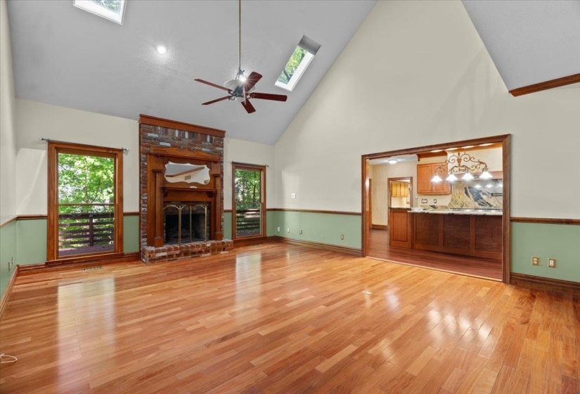 Unfurnished living room with high vaulted ceiling, light wood-style floors, a brick fireplace, healthy amount of natural light, and a ceiling fan