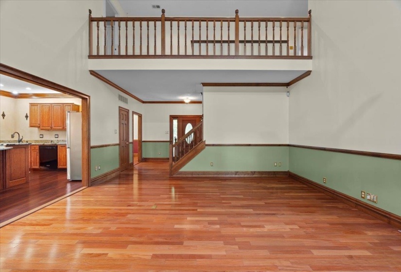 Unfurnished living room featuring light wood finished floors, stairs, crown molding, and a high ceiling