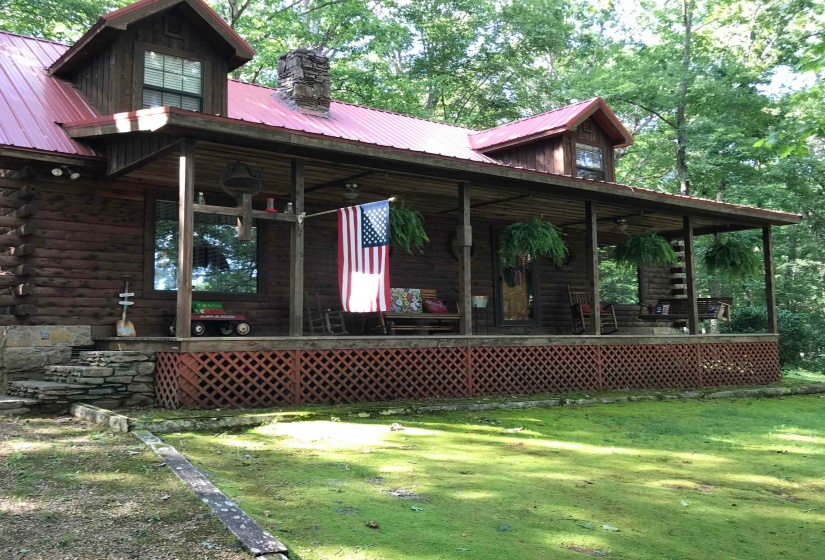 Front view of property featuring a large porch, log siding, a metal roof, a chimney, and a yard