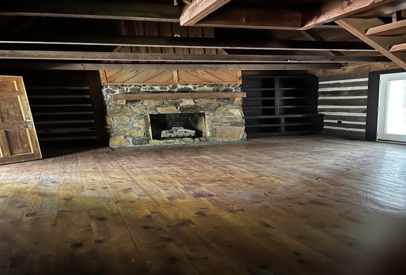 Unfurnished living room featuring beamed ceiling, hardwood / wood-style flooring, and a stone fireplace