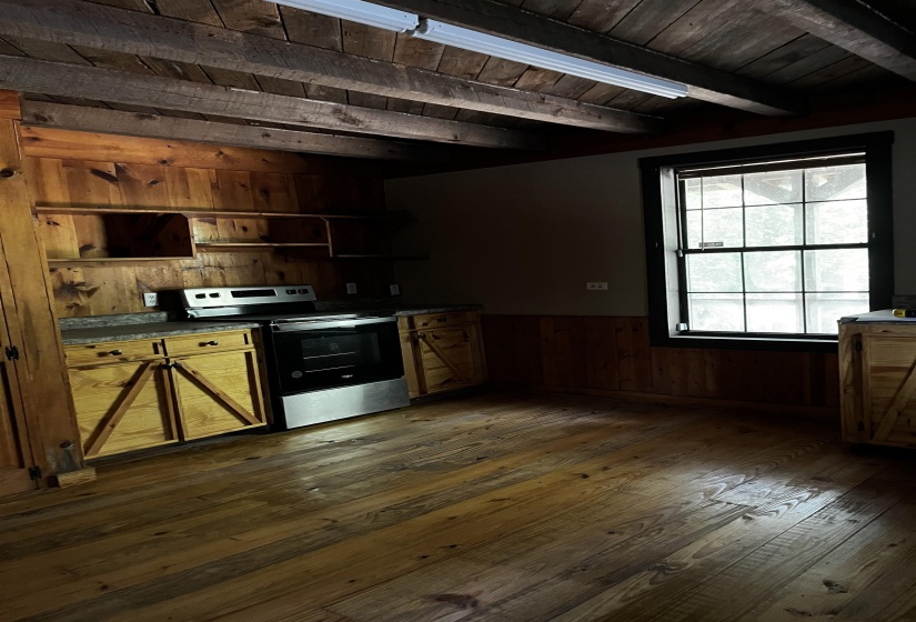 Kitchen with wooden walls, wainscoting, stainless steel electric range, dark wood-style floors, and a wooden ceiling with exposed beams