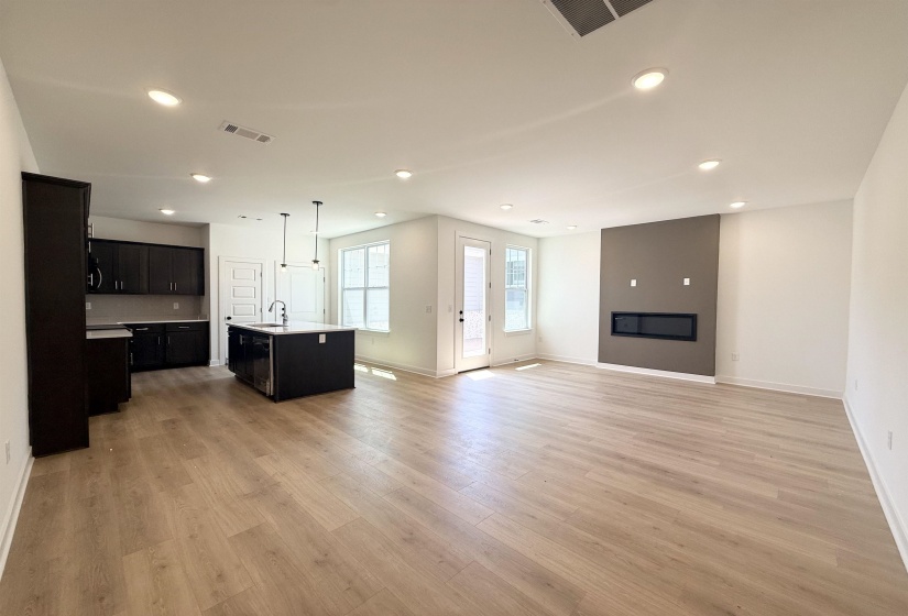 Kitchen featuring dark cabinetry, open floor plan, an island with sink, light wood-style floors, and pendant lighting