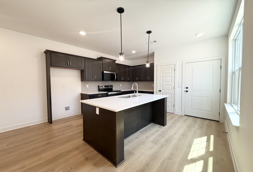 Kitchen featuring dark wood finish cabinetry, stainless steel appliances, light wood-style floors, an island with sink, and decorative light fixtures