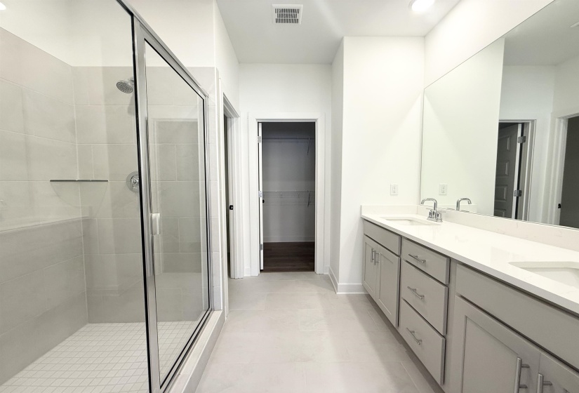 Bathroom featuring double vanity, a stall shower, a walk in closet, and light tile patterned floors