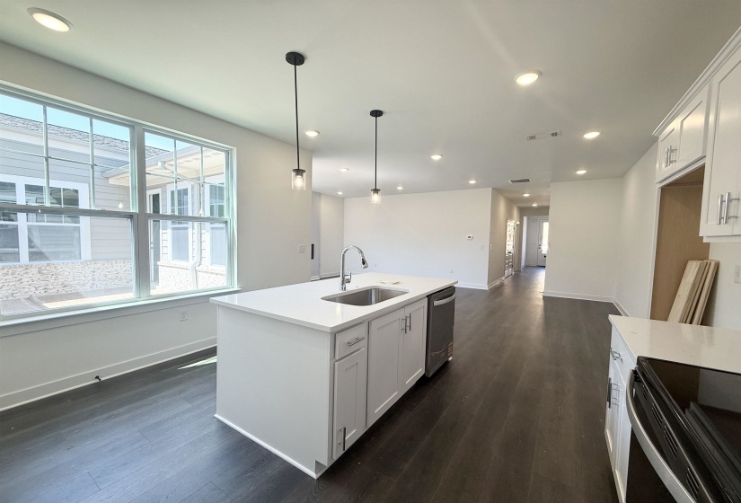 Kitchen with white cabinets, dark wood-type flooring, an island with sink, decorative light fixtures, and stainless steel appliances