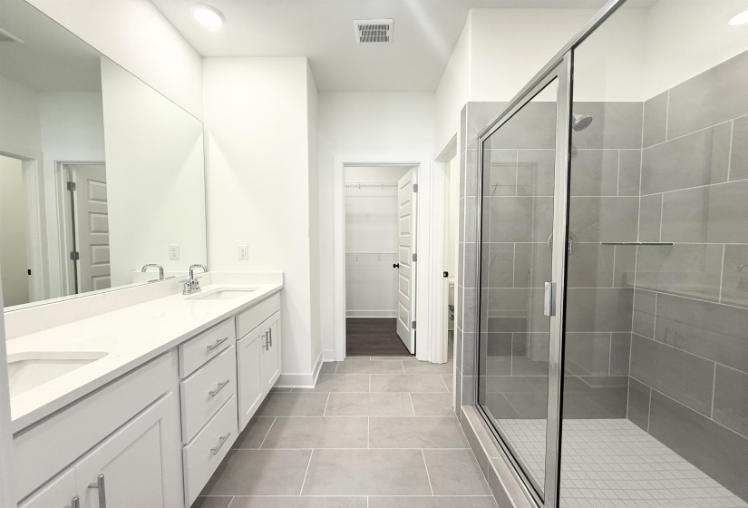 Full bath with double vanity, a walk in closet, a shower stall, light tile patterned floors, and recessed lighting