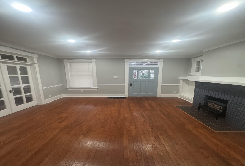 Unfurnished living room featuring dark wood finished floors, crown molding, and a brick fireplace