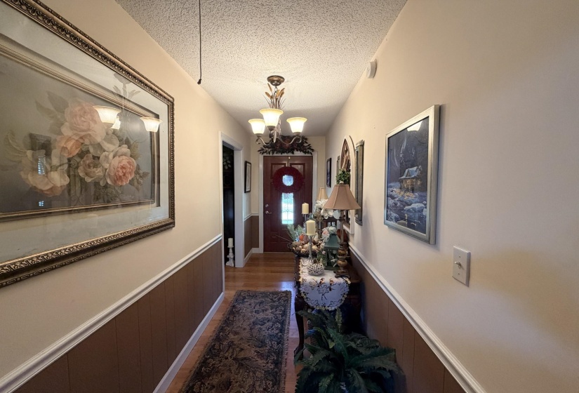 Hallway with wainscoting, a textured ceiling, a chandelier, and dark wood finished floors