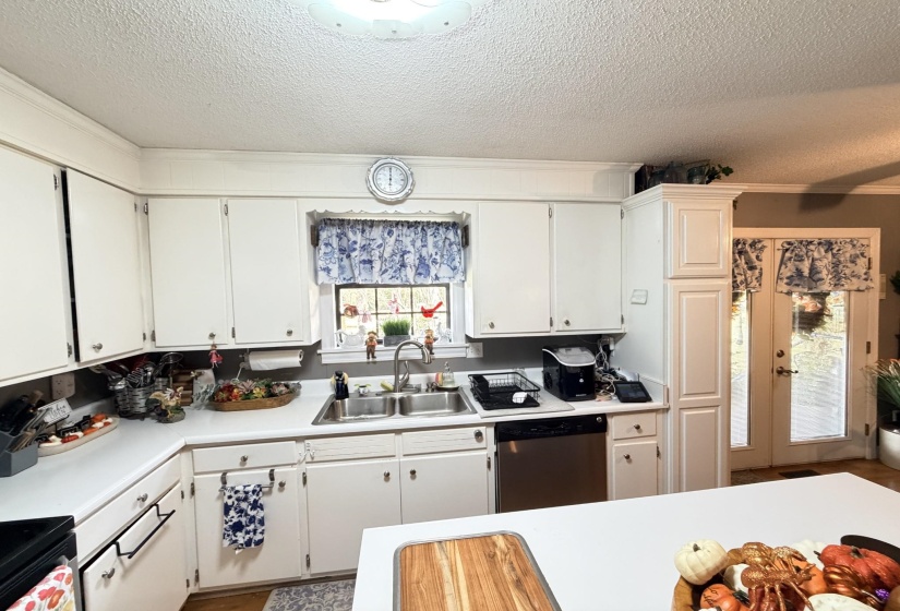 Kitchen featuring a textured ceiling, light countertops, white cabinetry, stainless steel dishwasher, and ornamental molding