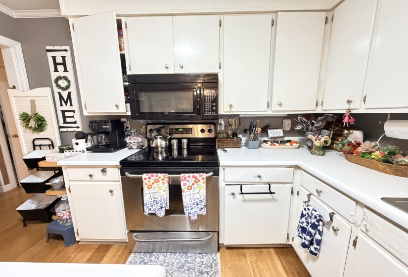 Kitchen featuring white cabinetry, light countertops, stainless steel electric range oven, black microwave, and ornamental molding
