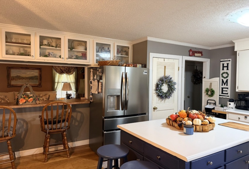 Kitchen with a kitchen bar, stainless steel fridge, light countertops, a textured ceiling, and white cabinetry
