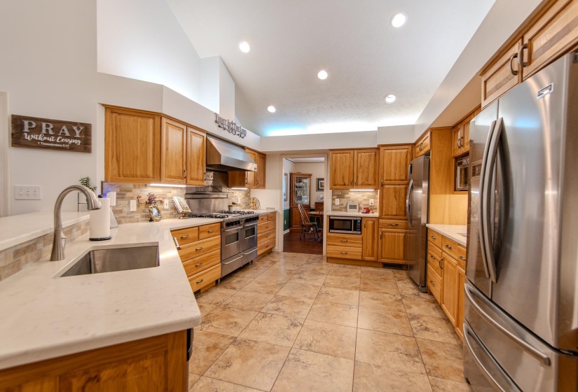 Kitchen featuring appliances with stainless steel finishes, tasteful backsplash, wall chimney exhaust hood, recessed lighting, and light stone countertops