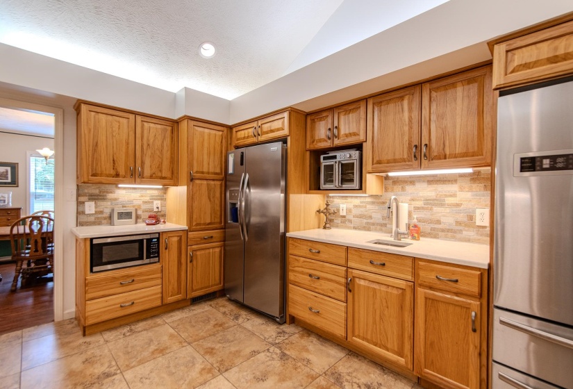 Kitchen featuring stainless steel appliances, backsplash, a textured ceiling, lofted ceiling, and brown cabinetry