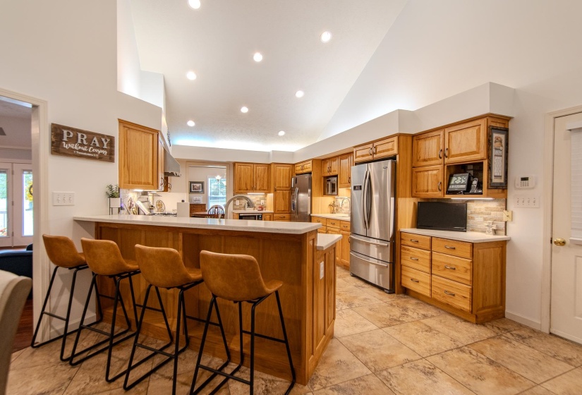 Kitchen with a kitchen breakfast bar, a peninsula, freestanding refrigerator, high vaulted ceiling, and recessed lighting